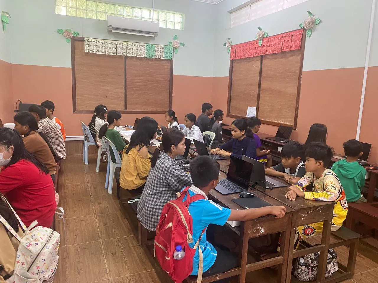 Students seated at wooden desks working on laptops in a classroom at New Hope School in Siem Reap